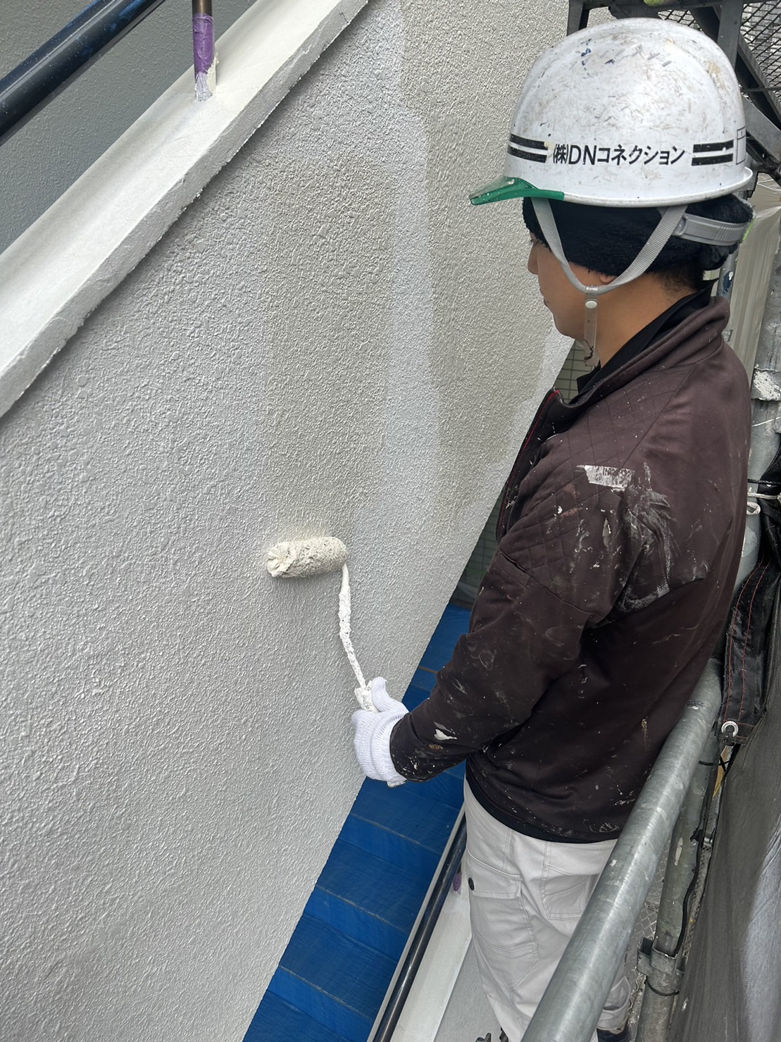 DNコネクションのヘルメットを着用し、横浜市の現場で外壁塗装作業を行うスタッフ